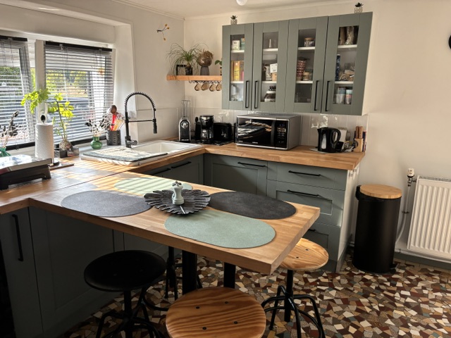 La cuisine après les travaux : façades vert sauge, plan de travail en bois massif, bar avec tabourets et électroménager encastré.