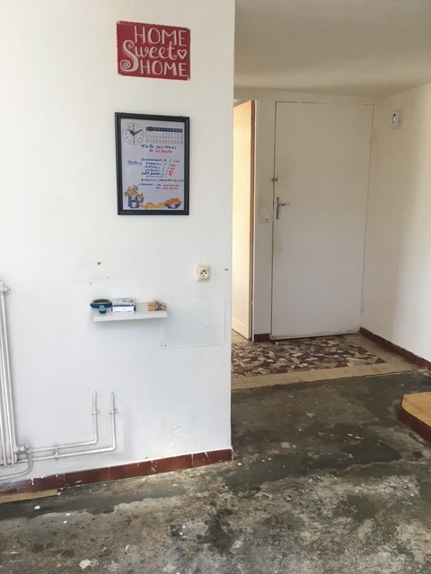 L'entrée avant les travaux : murs blancs marqués, sol en béton abîmé, tuyaux apparents.