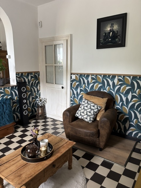 Le salon après les travaux : sol damier noir et blanc, papier peint à feuillage bleu et doré, soubassement bois et fauteuil club en cuir.